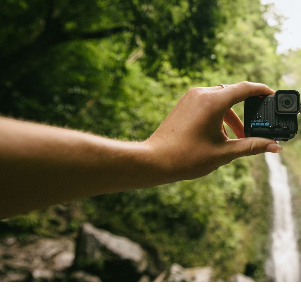 alAsil GoPro HERO 2024 action camera held in a hand against a lush forest waterfall background