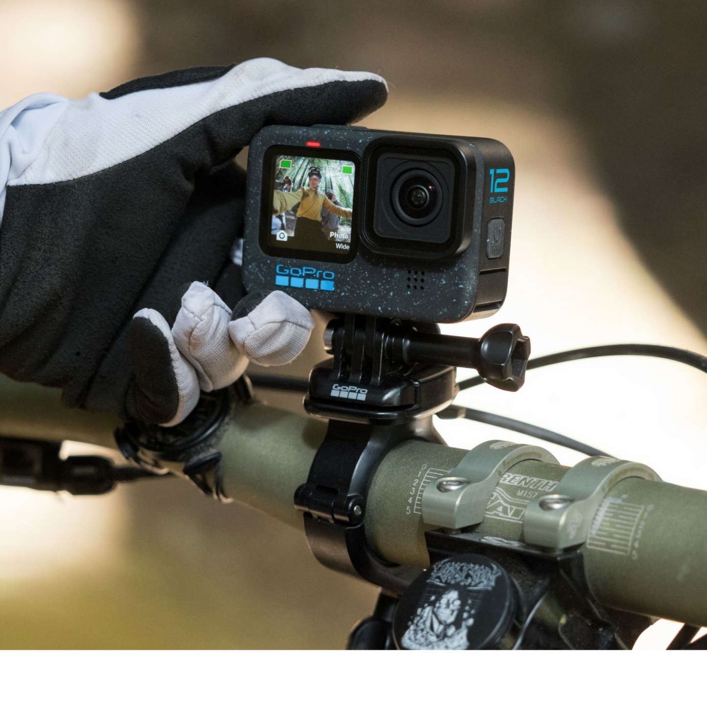 alAsil GoPro HERO12 Black action camera mounted on a bicycle handlebar, held by a gloved hand showing the front screen.