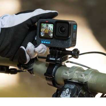 alAsil GoPro HERO12 Black action camera mounted on a bicycle handlebar, held by a gloved hand showing the front screen.