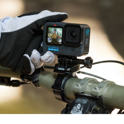 alAsil GoPro HERO12 Black action camera mounted on a bicycle handlebar, held by a gloved hand showing the front screen.