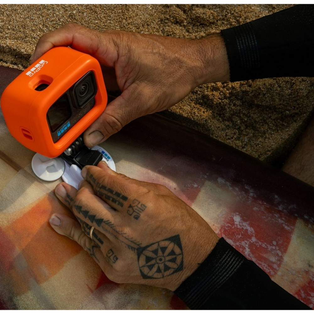 alAsil GoPro HERO12 Black action camera in an orange protective case being mounted to a surfboard on the beach.
