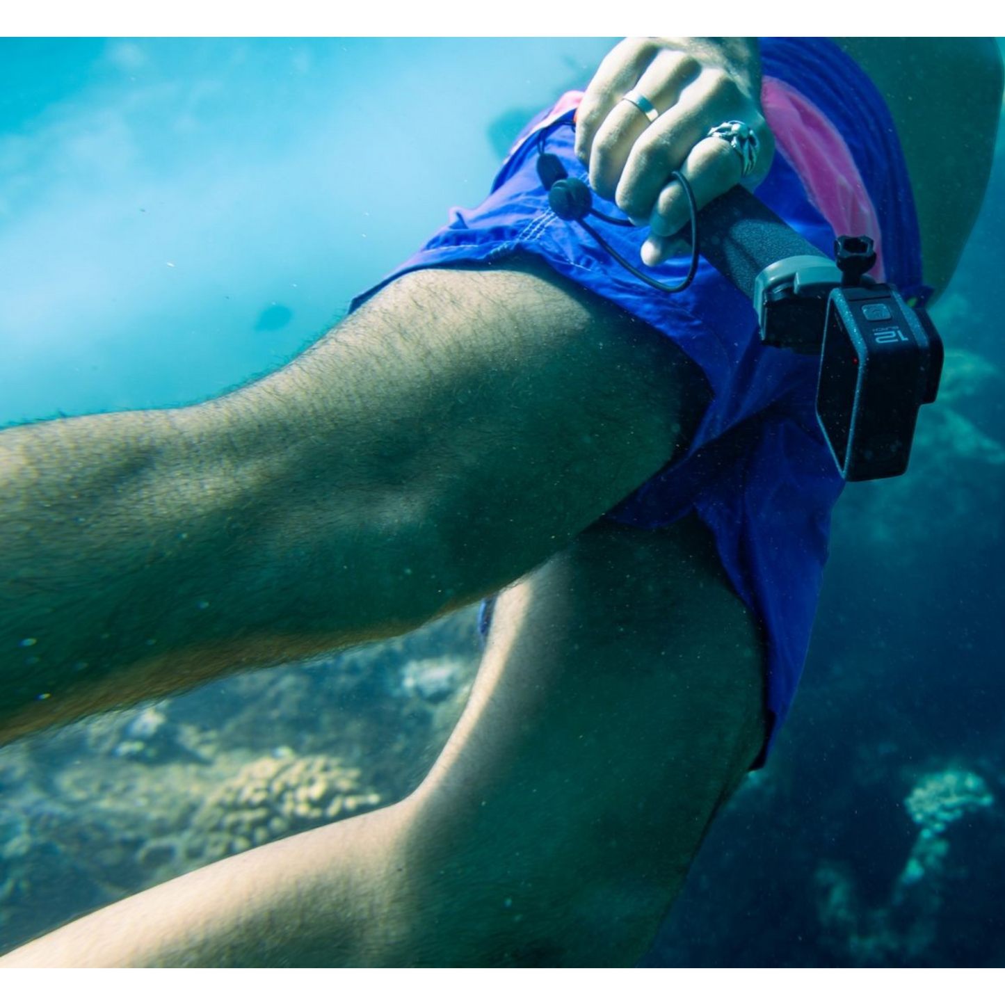 alAsil GoPro HERO12 Black action camera held underwater by a swimmer, capturing footage of a coral reef.