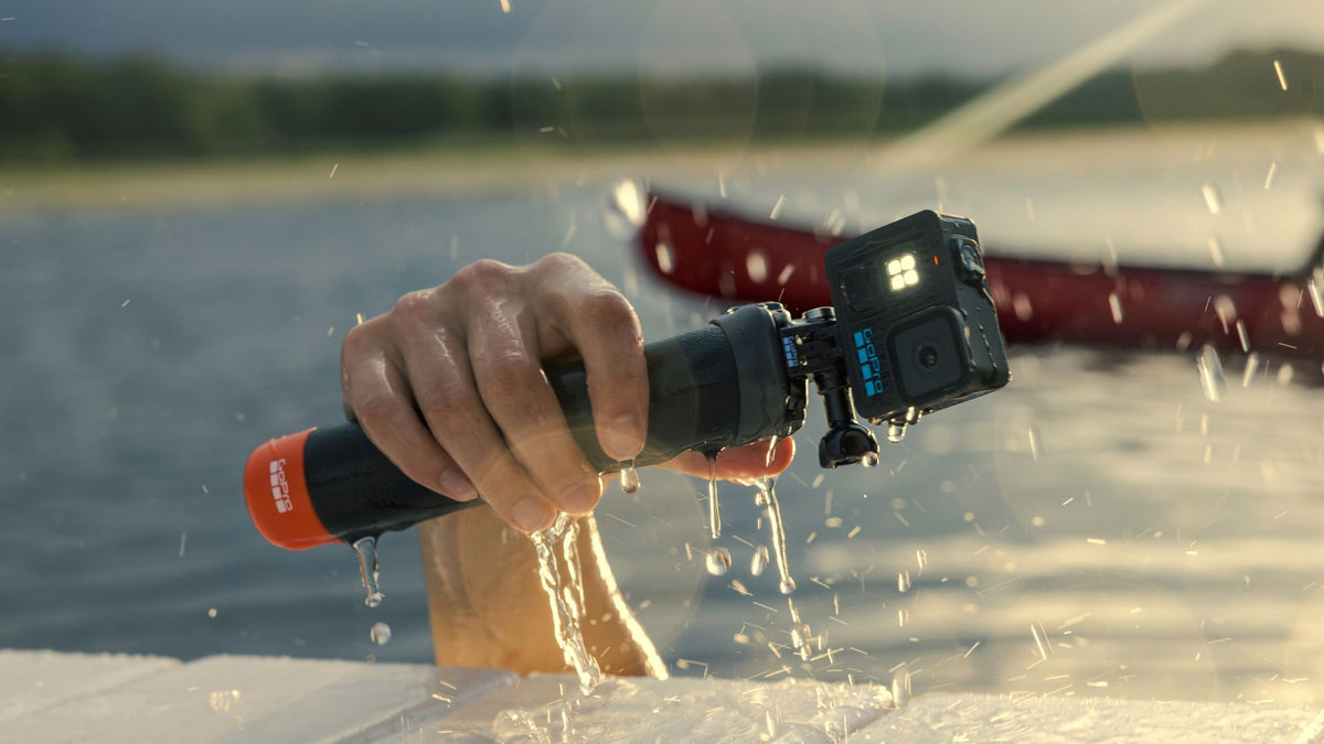 alAsil GoPro LIT HERO action camera with built-in light held over water, capturing 4K footage during outdoor activity.