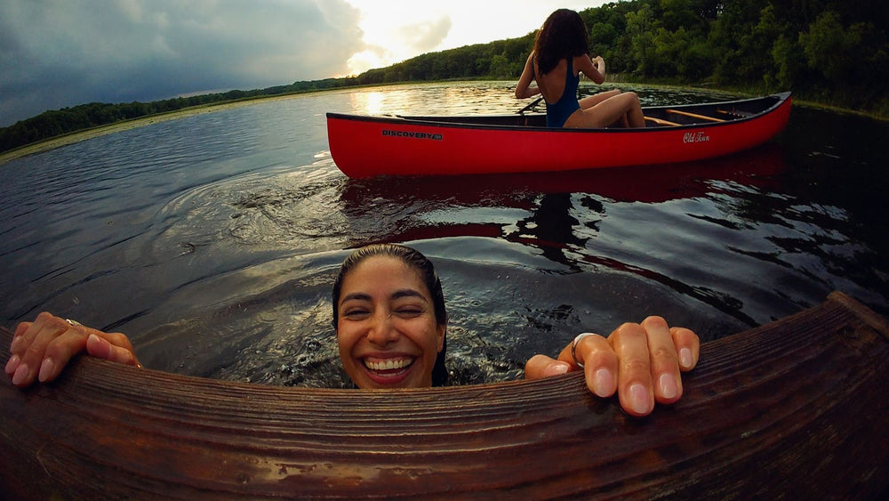 alAsil GoPro LIT HERO action camera capturing a smiling woman swimming in a lake with a red canoe in the background