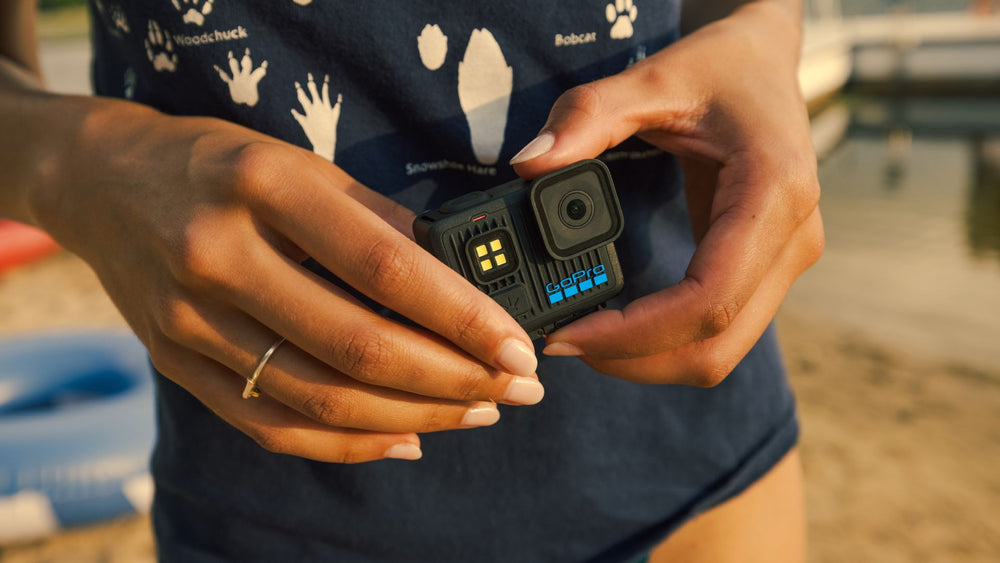alAsil GoPro LIT HERO action camera with built-in LED light held in hands at a beach during sunset