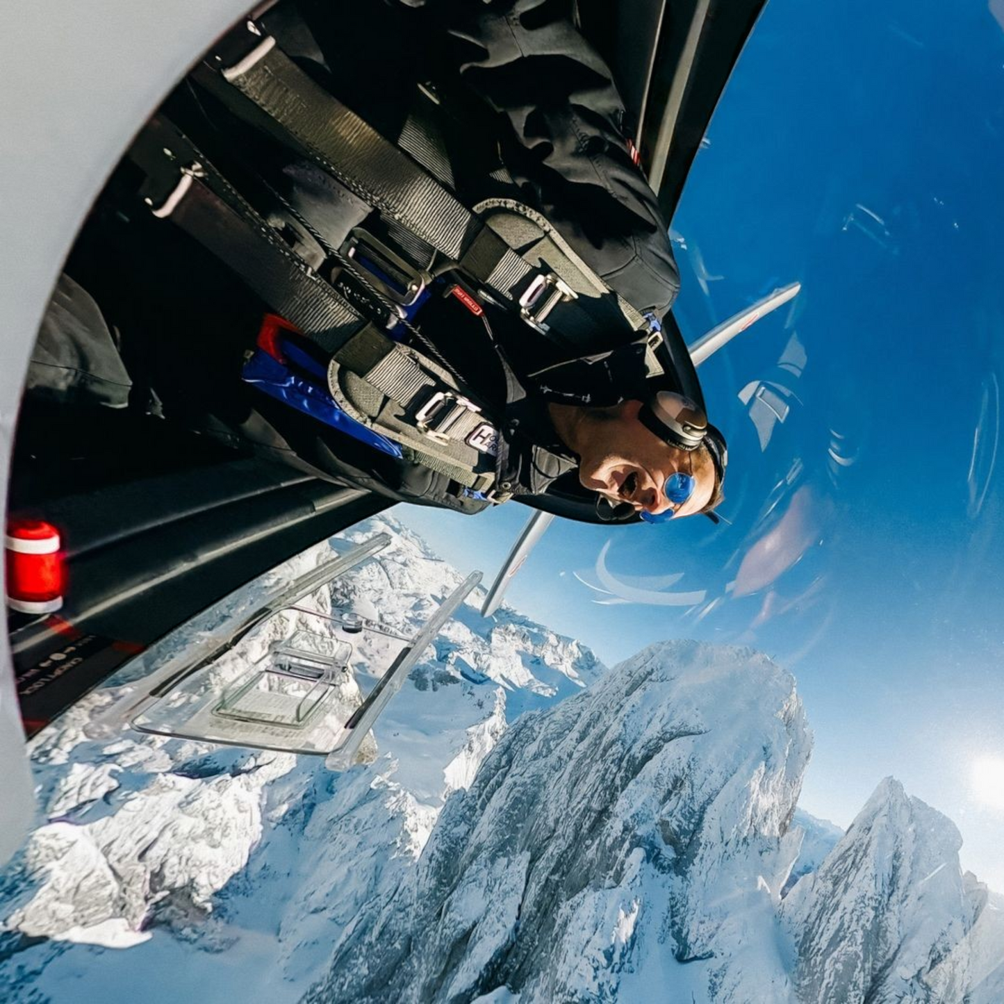 alAsil GoPro MAX2 360 camera captures a pilot in a helicopter cockpit flying over snow-capped mountain peaks.
