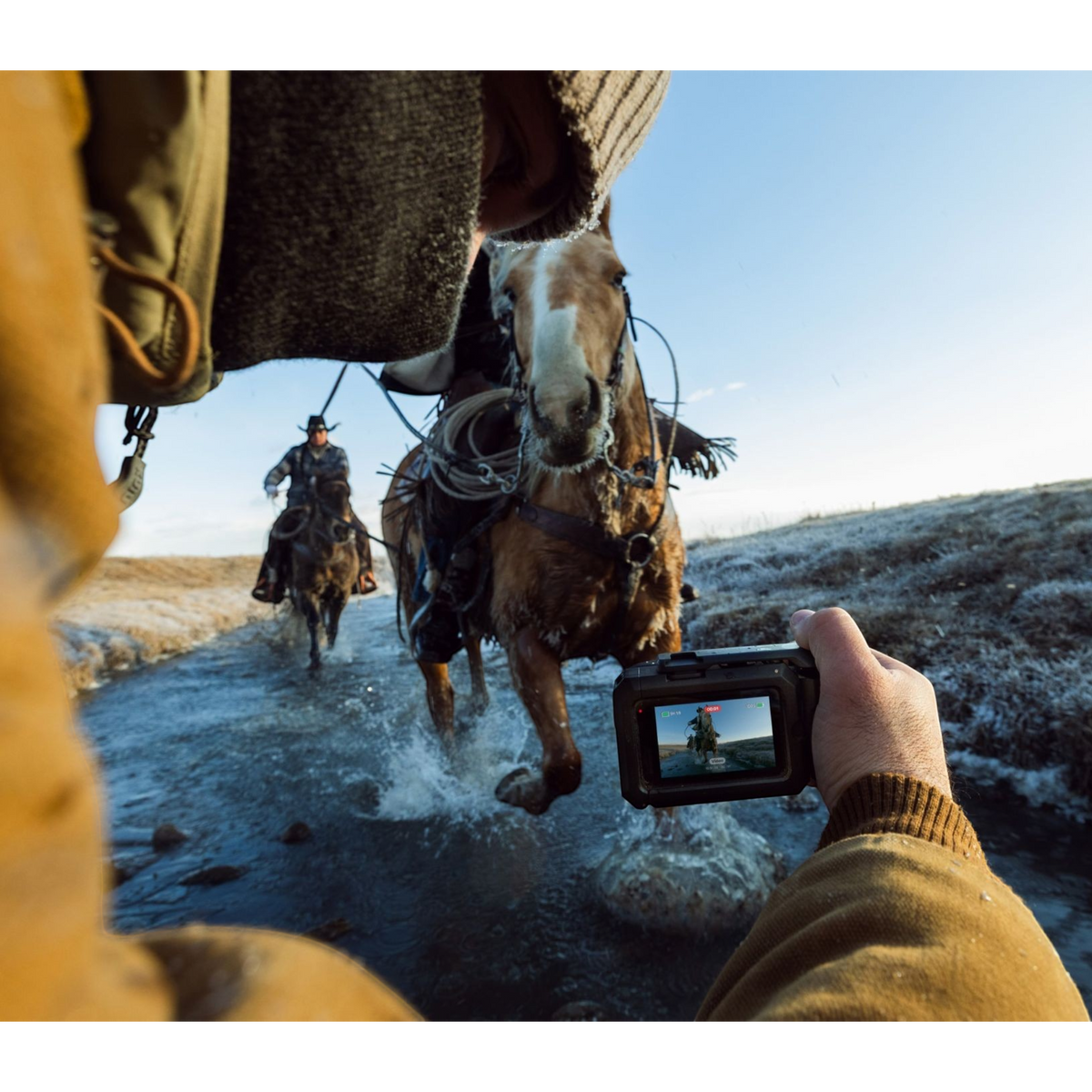 alAsil GoPro MISSION 1 PRO cinema camera held by a person filming a horse rider crossing a shallow stream at sunrise