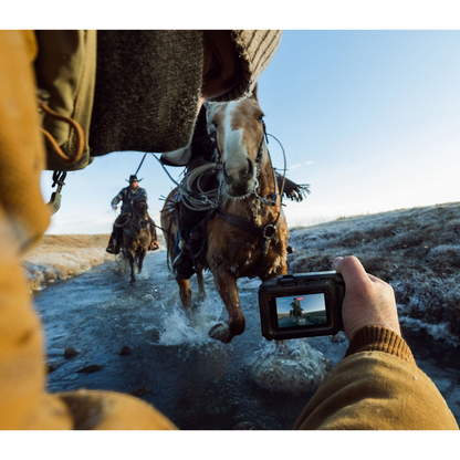 alAsil GoPro MISSION 1 PRO cinema camera held by a person filming a horse rider crossing a shallow stream at sunrise